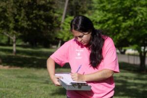 Gracie Oliver takes notes while standing outside in a pink shirt. 