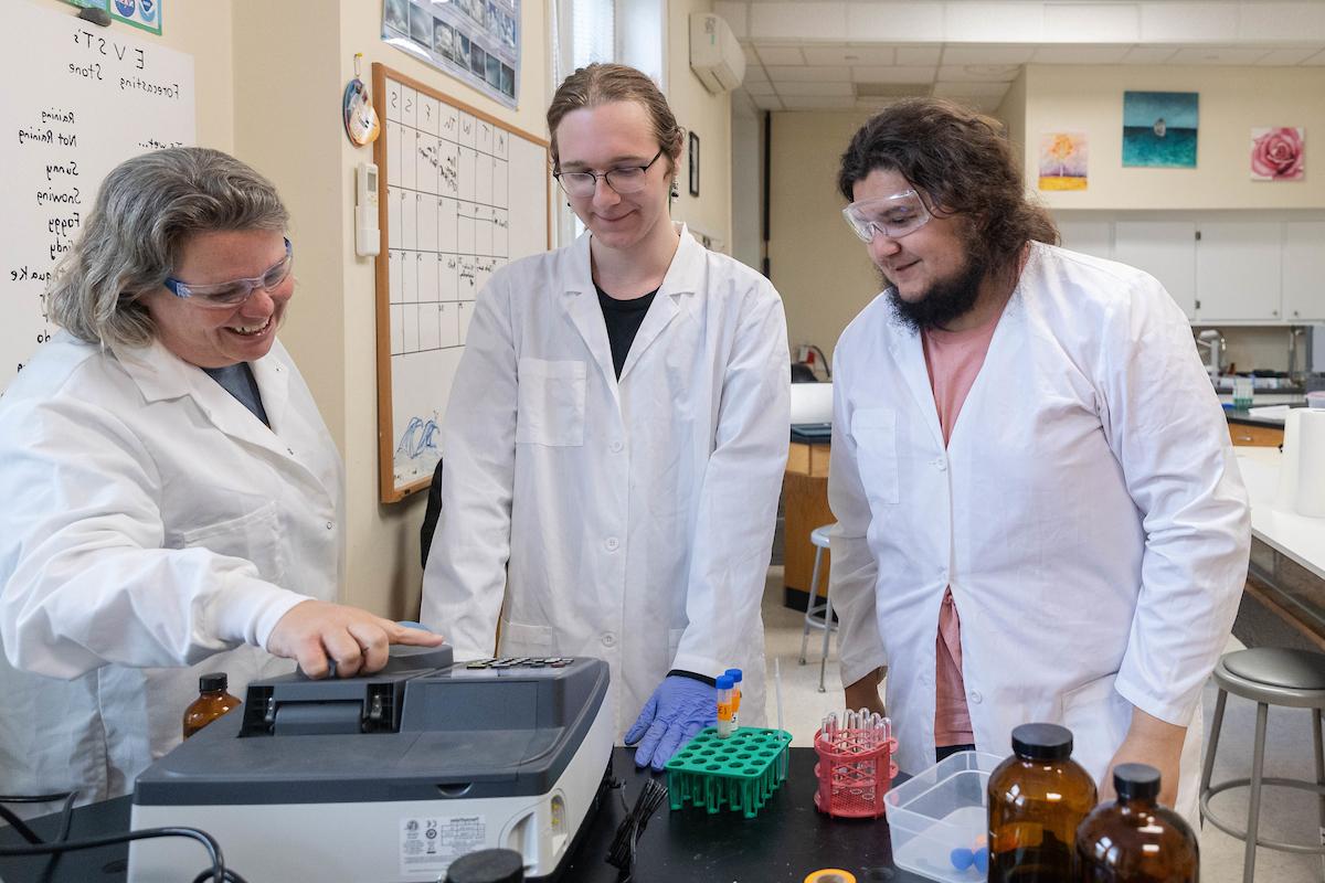 萨拉·索伊卡教授和两名学生在环境科学实验室的一台机器上分析读数