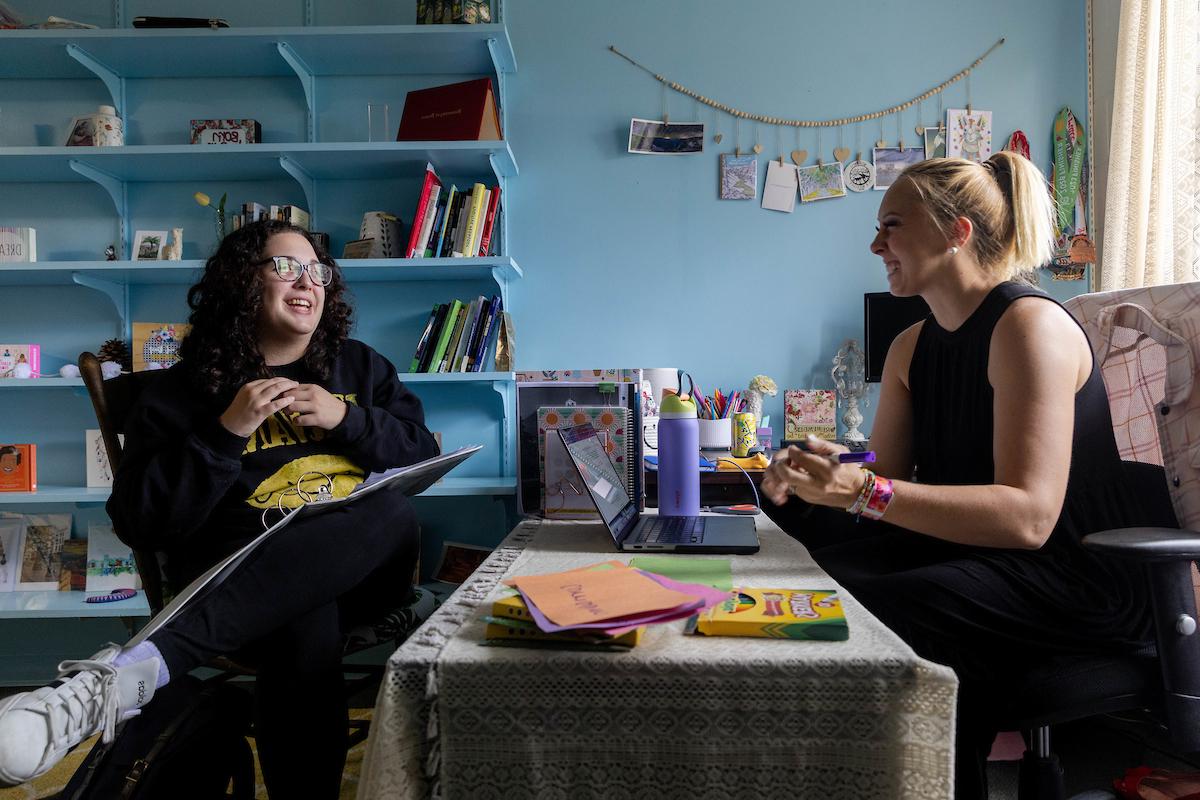 教育学教授世界罗伯逊说, 左, 和25岁的Madeline Dearie坐在Robertson的办公室里, 隔着她的桌子聊天. 
